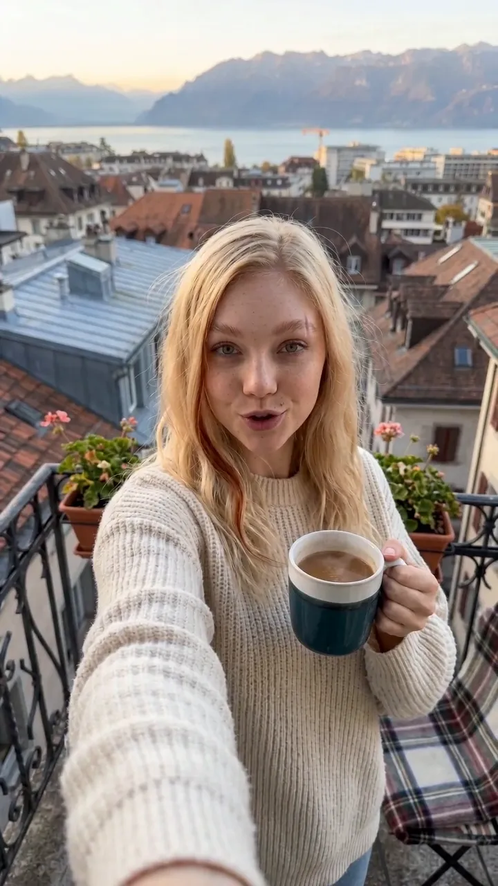 Katia Ryze, personnage généré par IA, filme un selfie avec une tasse de café sur un balcon au-dessus du Léman